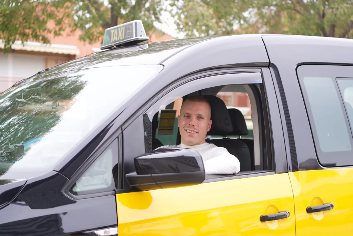 Conductor al volante de un taxi negro y amarillo, visto desde la ventanilla.